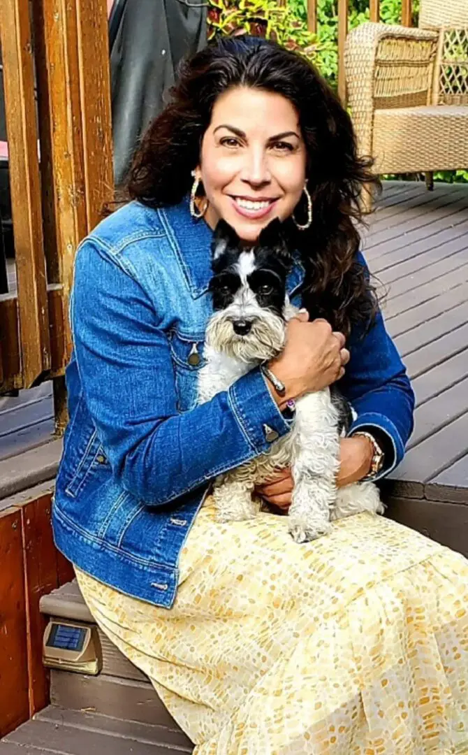 A woman holding her dog on the porch.